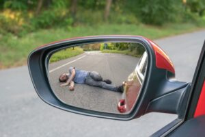 Hit-and-run concept: A rearview mirror reflects the image of an injured man lying on the road, emphasizing the tragedy of fleeing the accident scene.