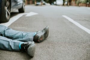 An individual lying injured on the ground following a car accident, highlighting the seriousness of road safety and the need for immediate assistance.