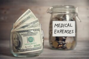 Dollars and coins in a glass jar with a "Medical Expenses" label, representing a financial concept. Vintage toned wooden background with dramatic lighting.