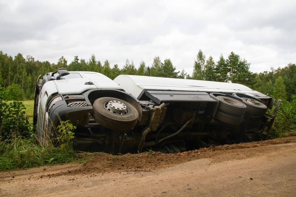 A truck overturned on its side following a road accident, surrounded by debris and emergency responders assessing the scene.