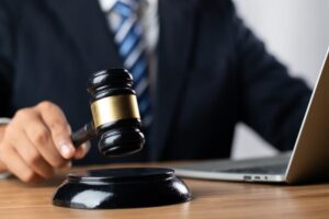 Justice, law, and attorney concept: A judge holds a gavel poised above a sounding block in a courtroom, symbolizing authority and decision-making.