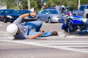 A motorcycle rider has been wrecked and is lying in the road as his bike slides into the busy intersection.