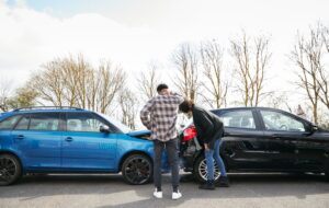 A young man and woman examine the rear-end damage to a car following a traffic accident.