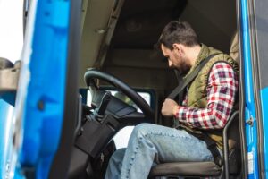 A young truck driver putting on his safety belt inside his truck. 