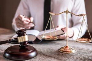 Male lawyer or judge in an office, surrounded by law books, a gavel, and a balance scale, reviewing a case report on the table, representing law and justice.