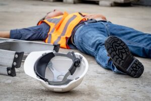 Construction site accident: Unconscious male worker lying on the floor with a safety helmet after falling from a ladder, highlighting the importance of safety and potential risks like exhaustion or heat stroke.