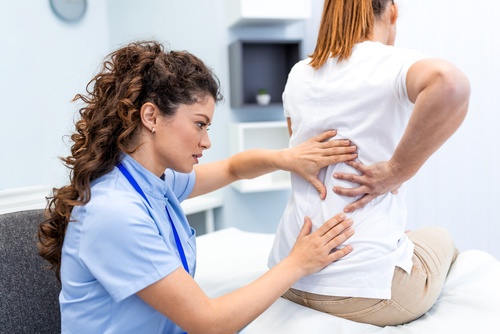 Female healthcare professional examining patient’s lower back during clinical spinal assessment