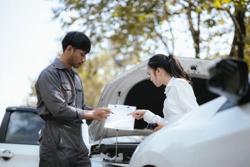 insurance agent and mechanic reviewing clipboard documents beside vehicle with open hood