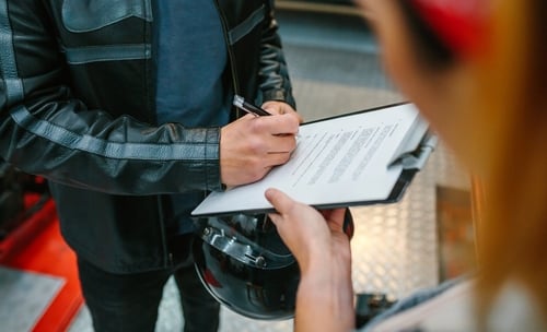 motorcyclist in leather jacket signing document on clipboard outdoors