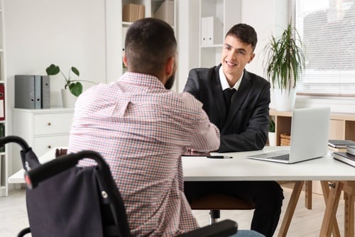 suited attorney meeting with wheelchair-using client across office desk with laptop