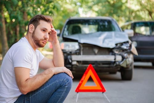 distressed man sitting near warning triangle sign and damaged vehicle after collision