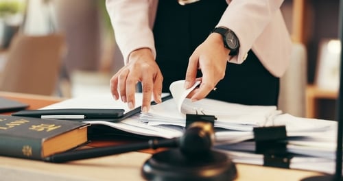 judge's hands reviewing stack of legal paperwork beside gavel on desk