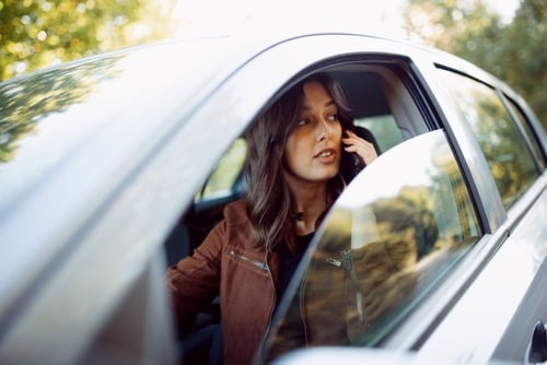 woman talking on cell phone while seated inside moving vehicle
